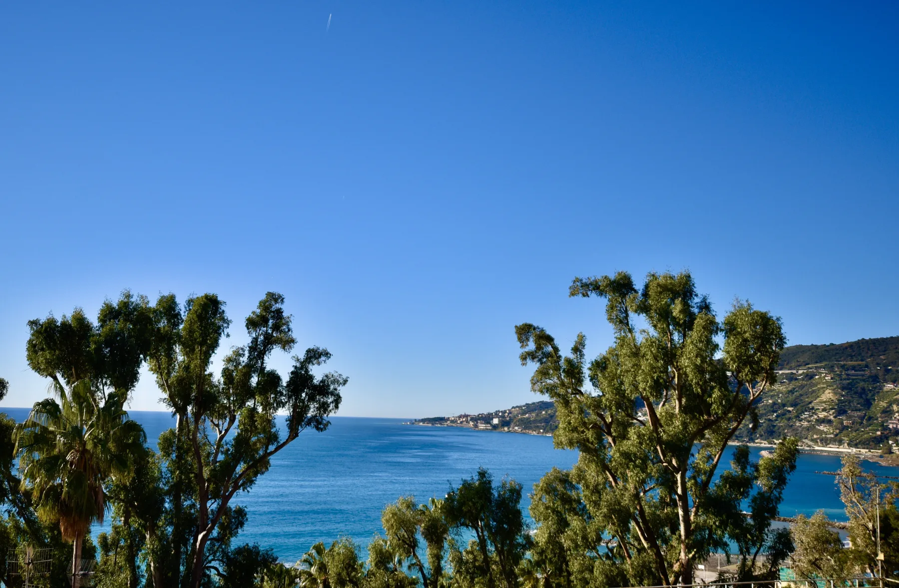 A coastal landscape with blue sea, green trees, and hills along the shoreline.