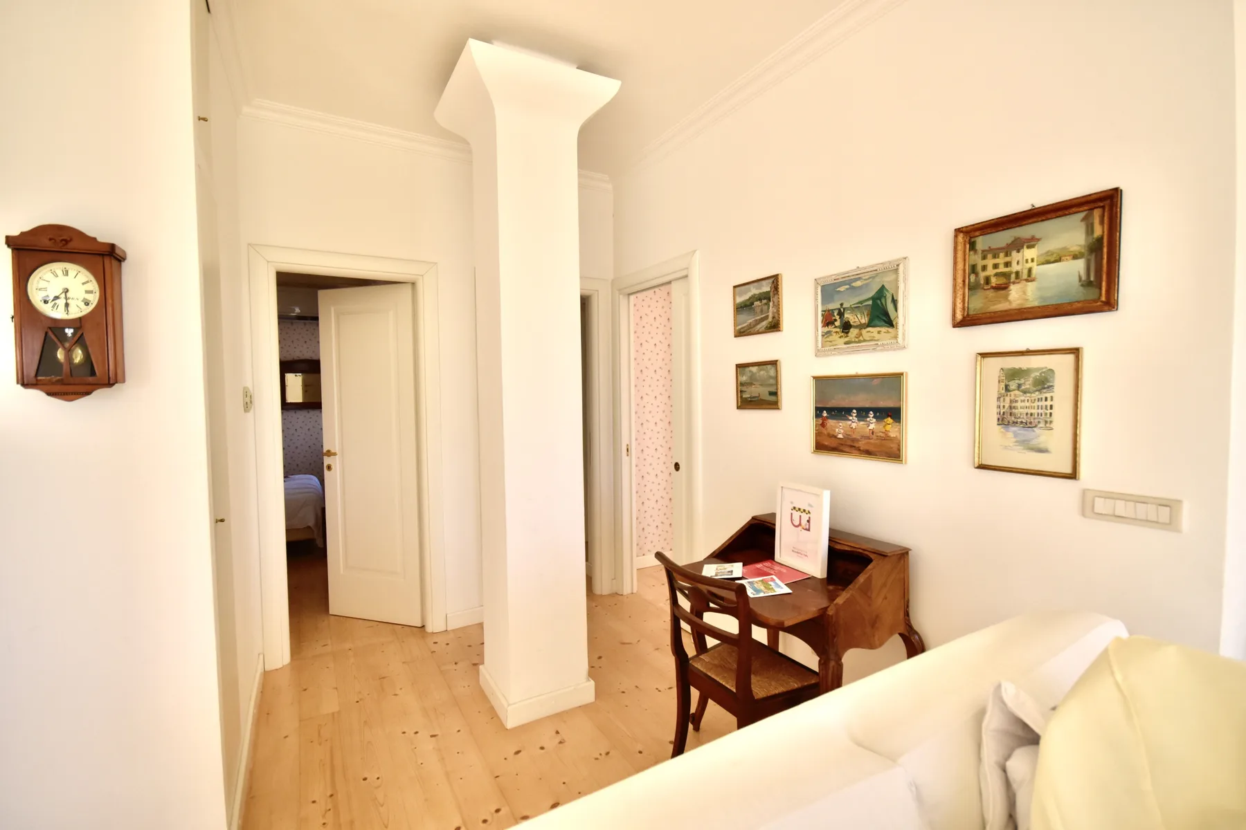 A bright interior room with a writing desk, framed pictures, and a doorway.