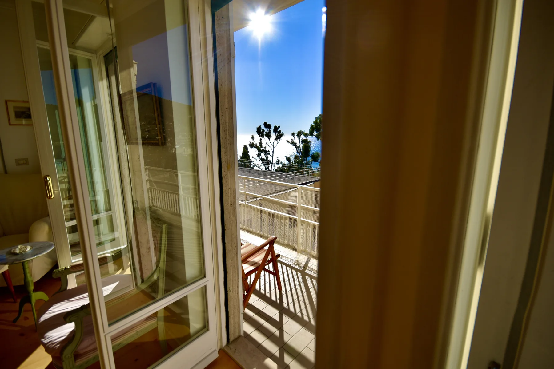 A bright balcony is visible through open glass doors, with outdoor seating and a railing.
