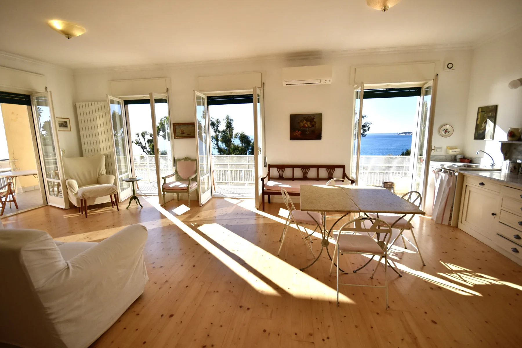A bright living and dining area with a table, seating, and open balcony doors.