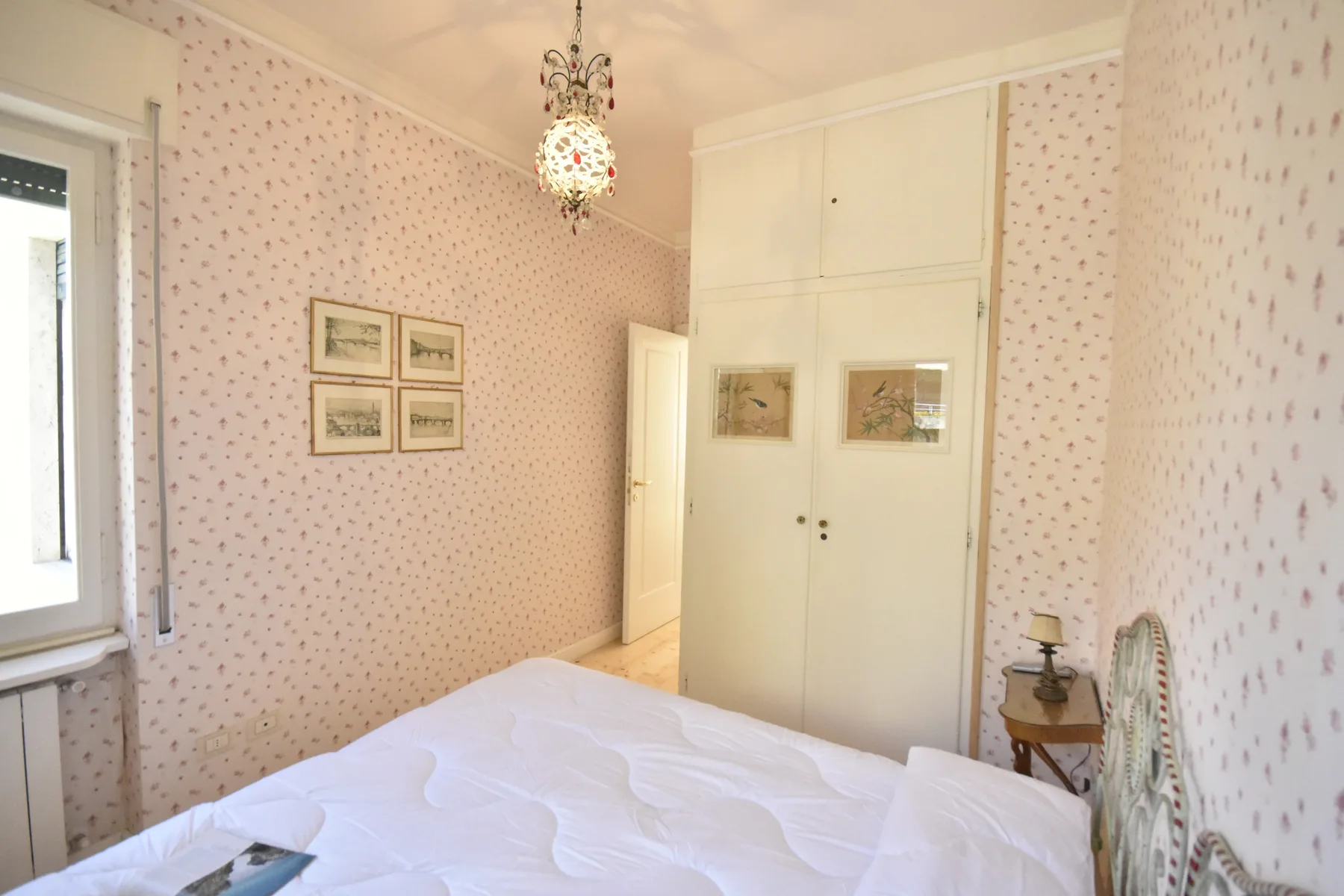 A bedroom with a bed, patterned wallpaper, and a white wardrobe.