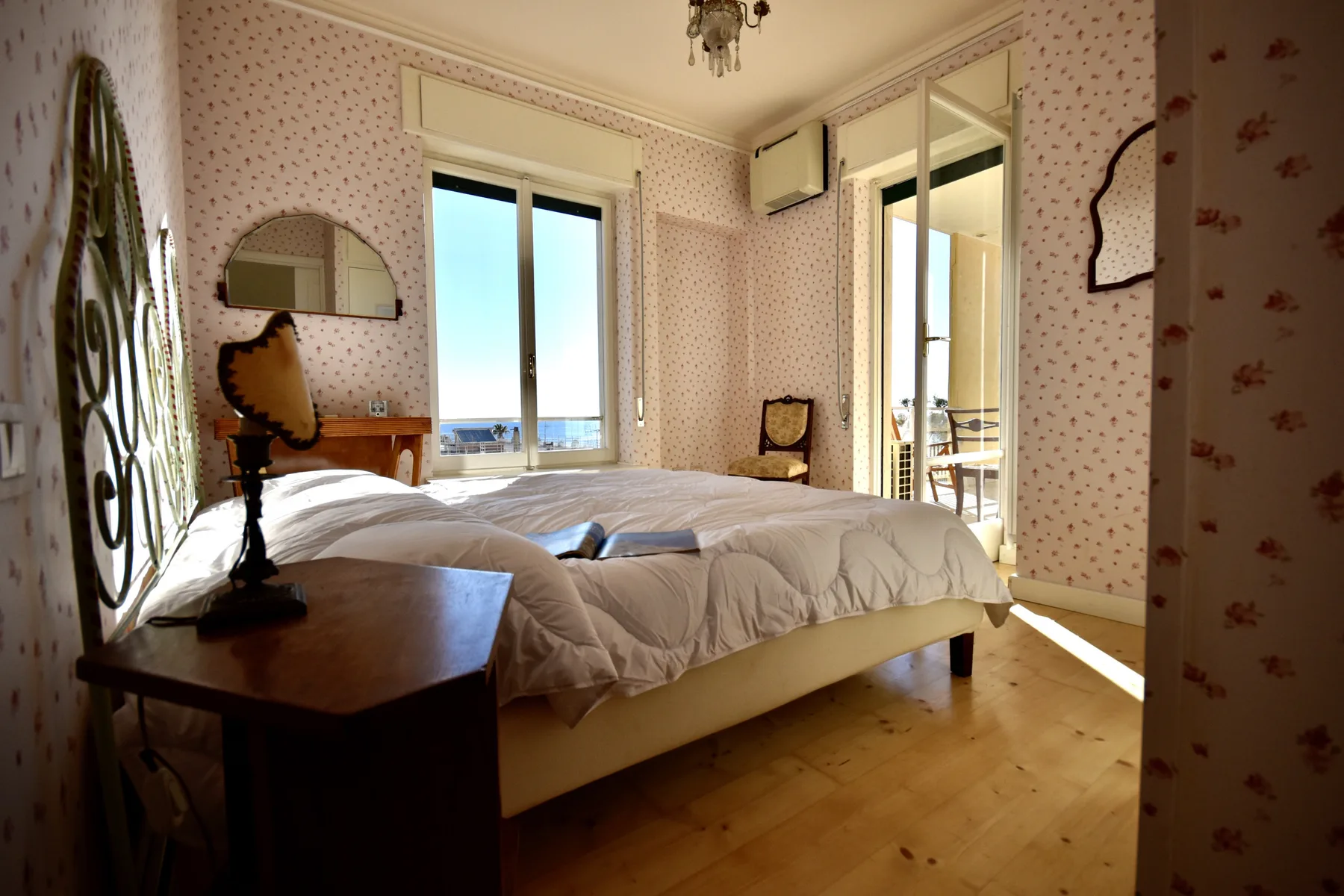 A bedroom with a double bed and tall windows letting in daylight.