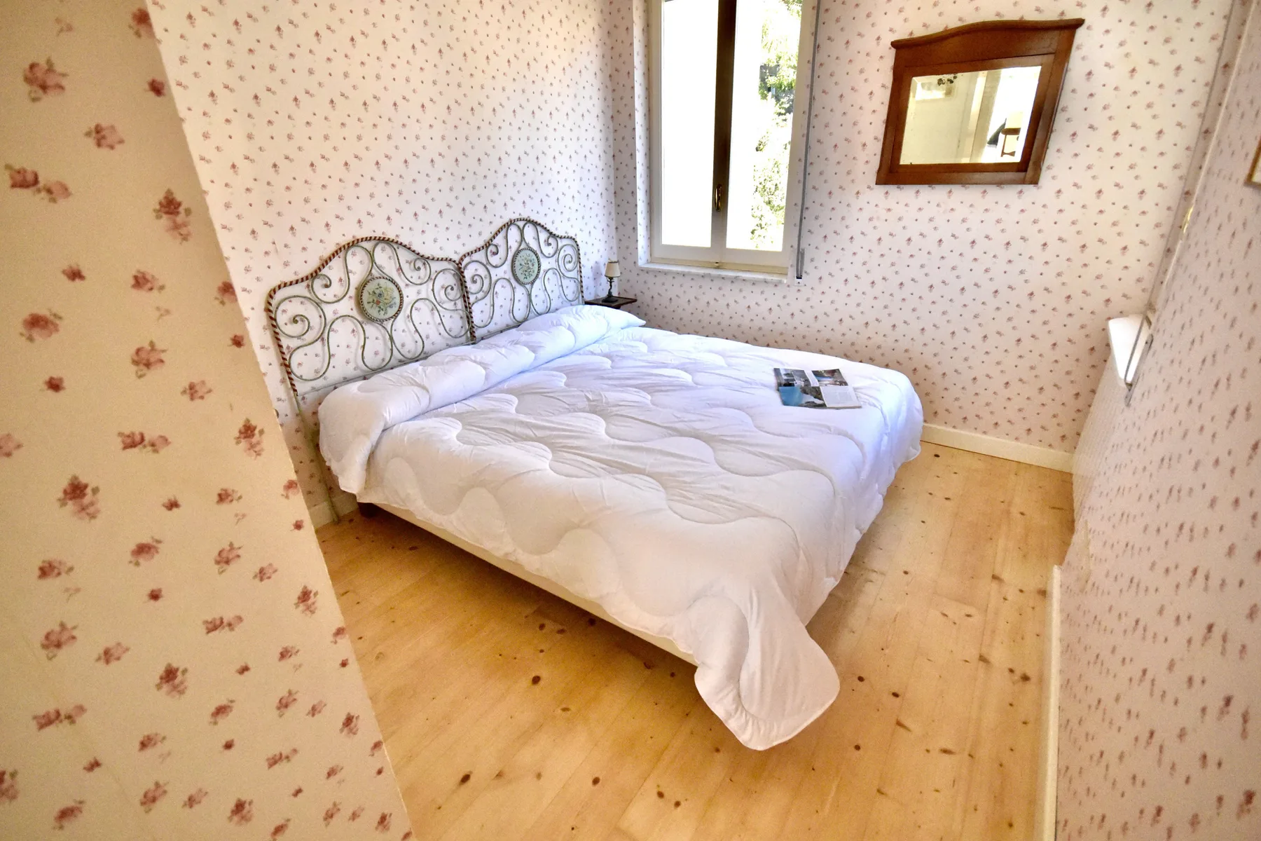A bedroom with a bed beneath a window and floral-patterned wallpaper.