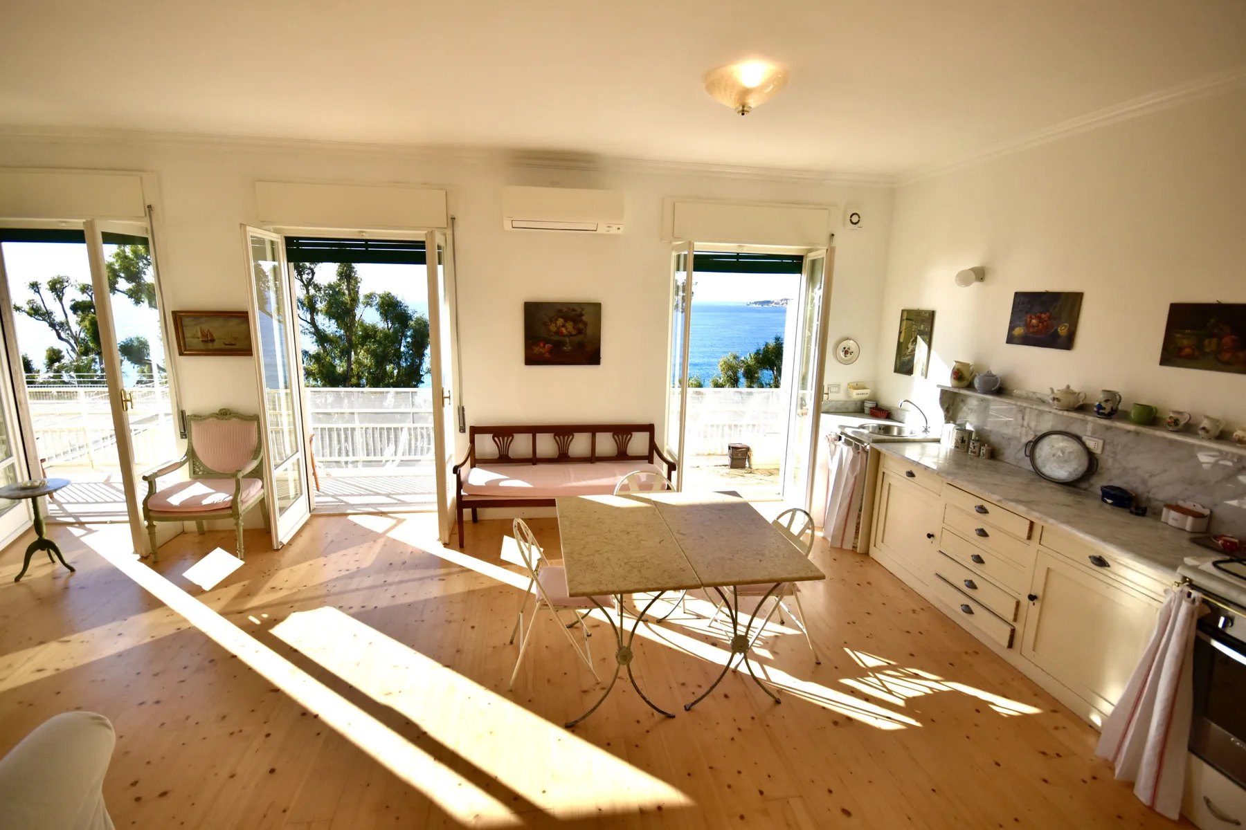 A sunlit dining room with a table, seating, and open doors to a balcony.