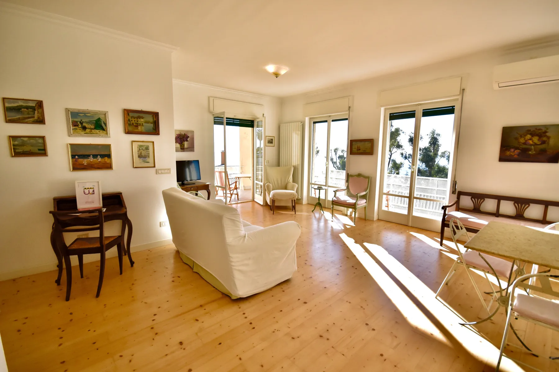 A bright living room with seating, framed pictures, and large windows.