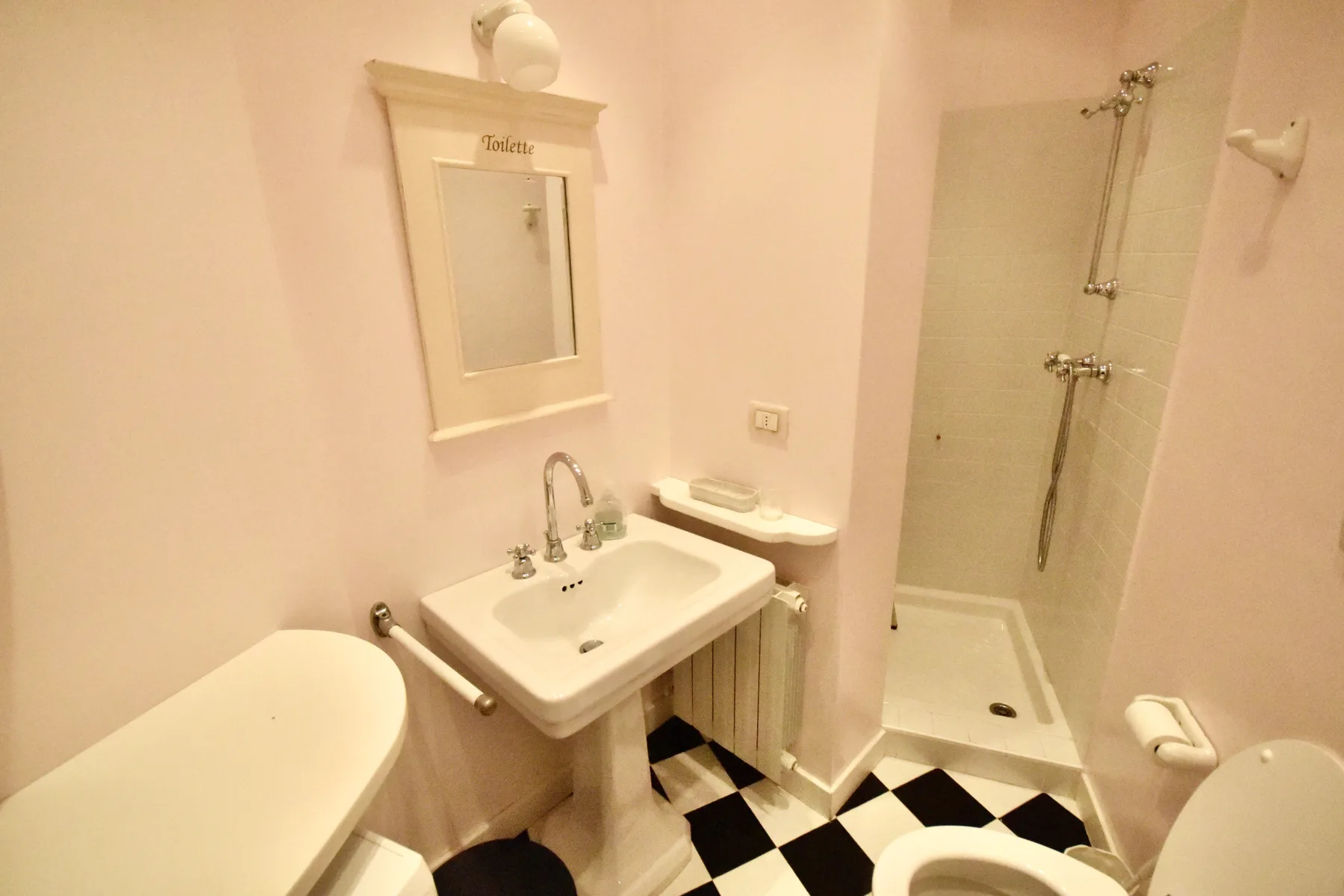 A bathroom with a pedestal sink, shower, and black-and-white tiled floor.