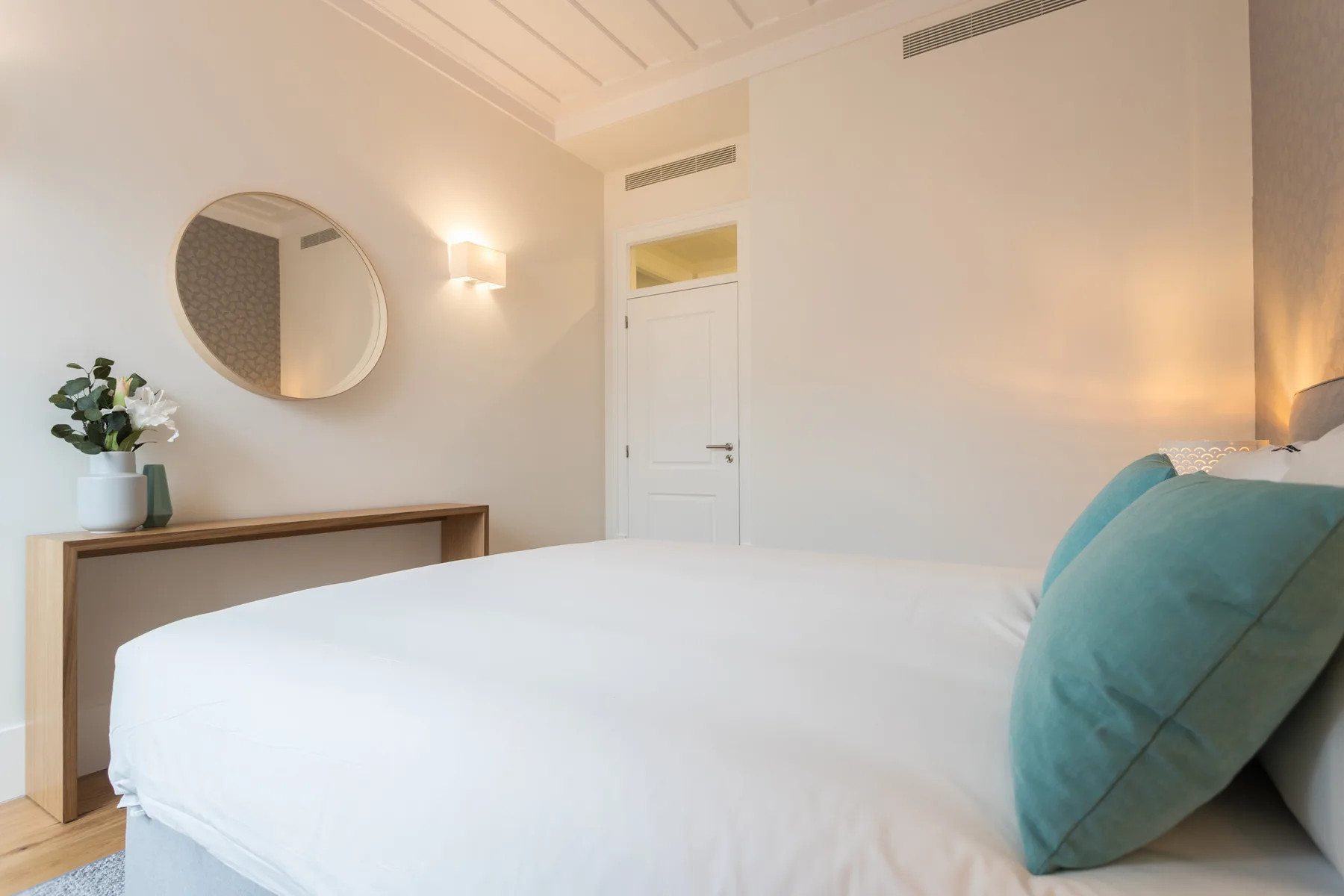 Un dormitorio luminoso con una cama bien hecha y almohadas turquesas.