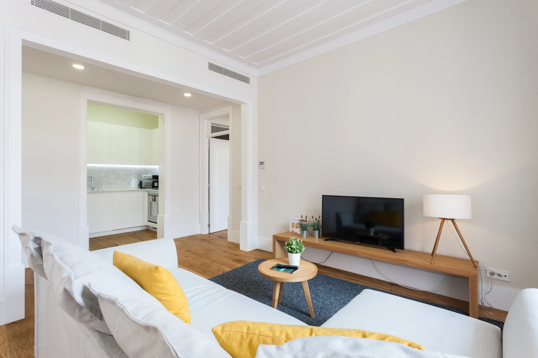 Una sala de estar luminosa con sofá, televisor y cocina abierta.