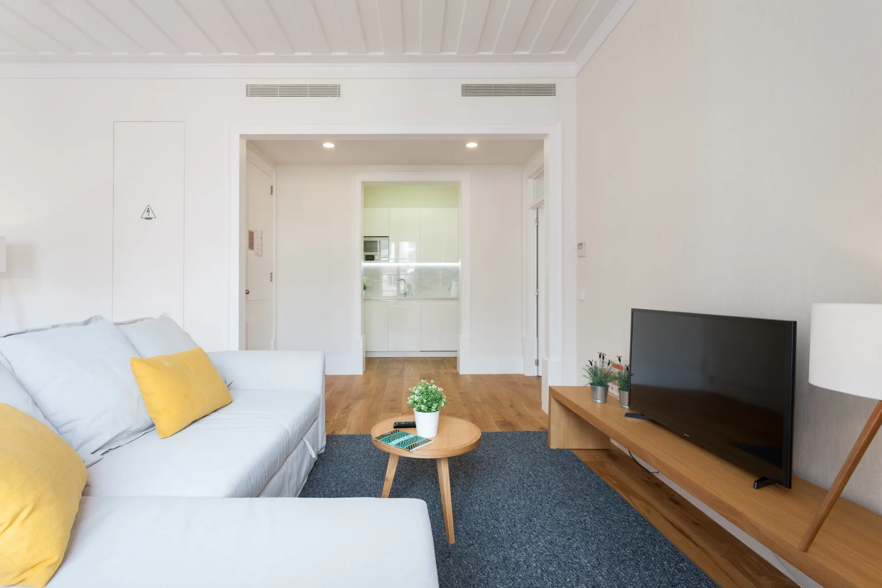 Sala de estar con asientos, un televisor y la cocina abierta al fondo.