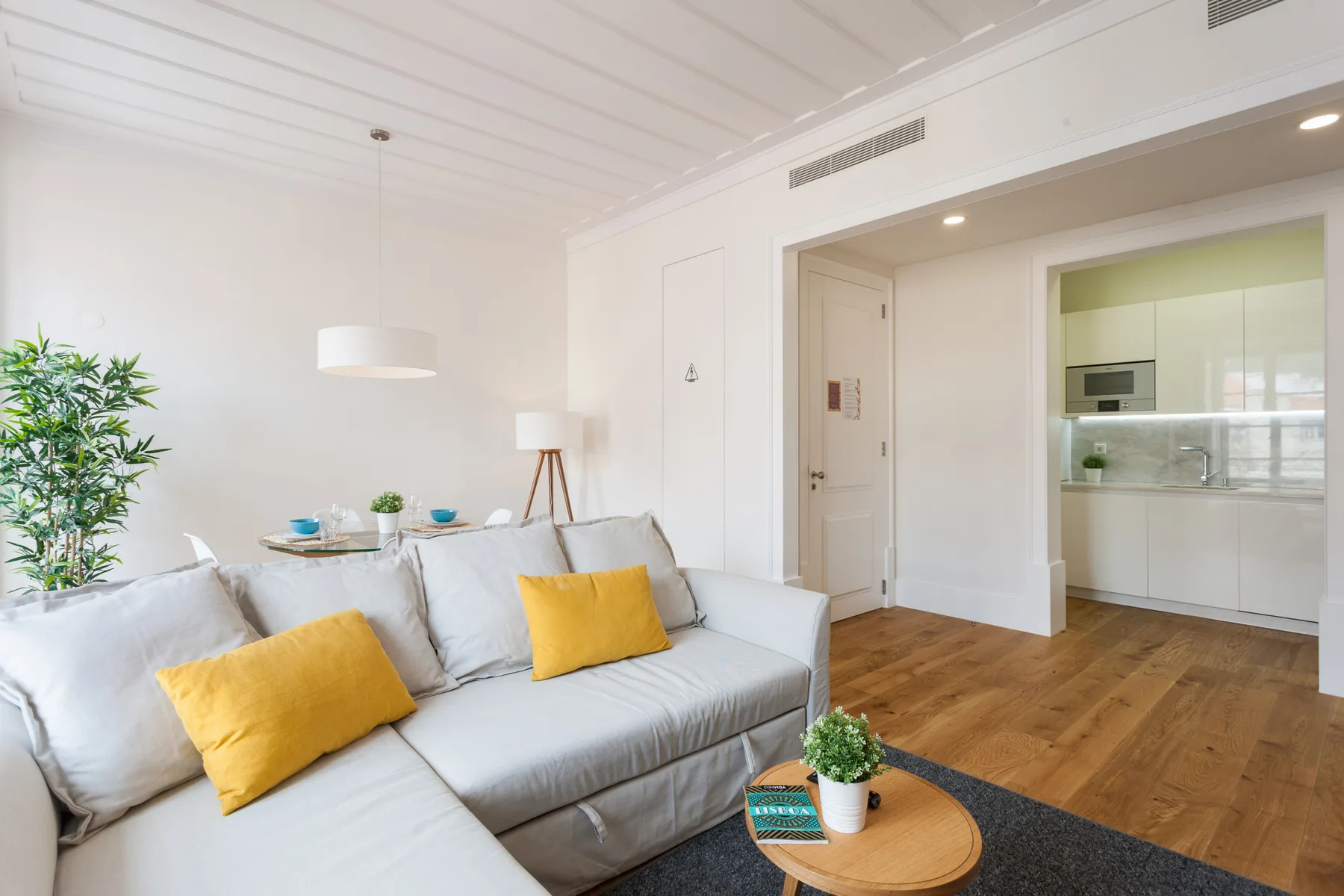 Una sala luminosa con asientos claros y una vista abierta hacia la cocina.