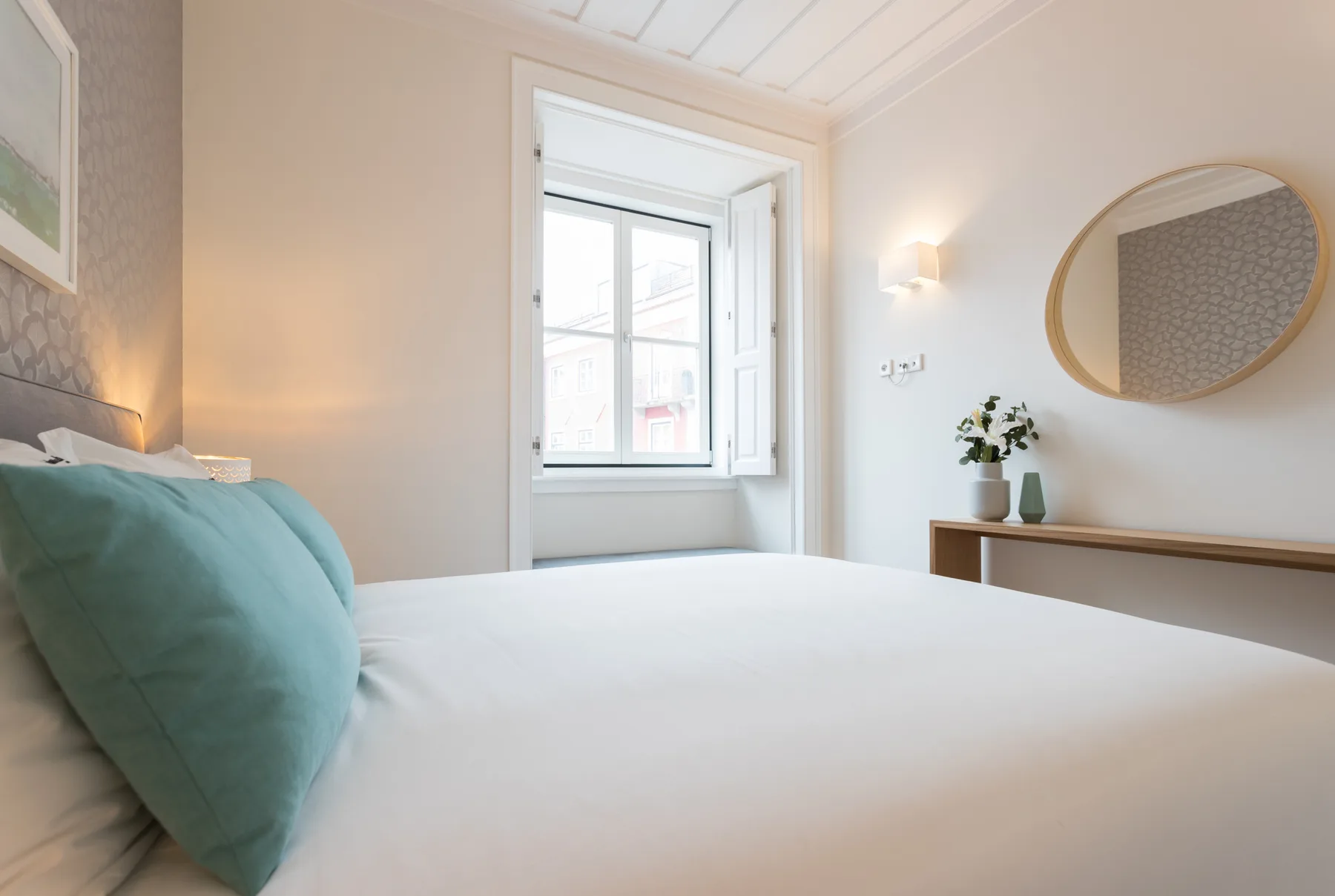 Dormitorio con una cama bien hecha, almohadas turquesas y una ventana grande.