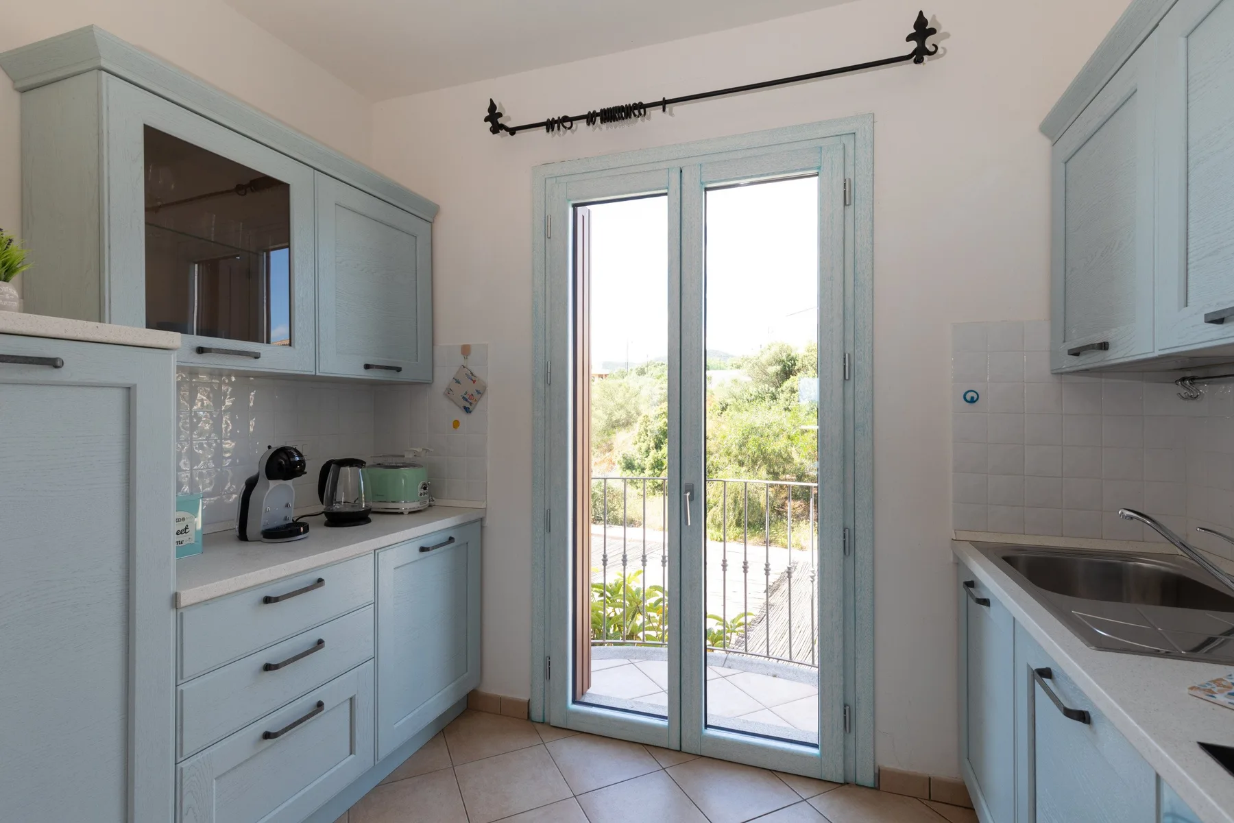 Una cocina luminosa con gabinetes azul claro y puertas de vidrio que dan a un balcón.