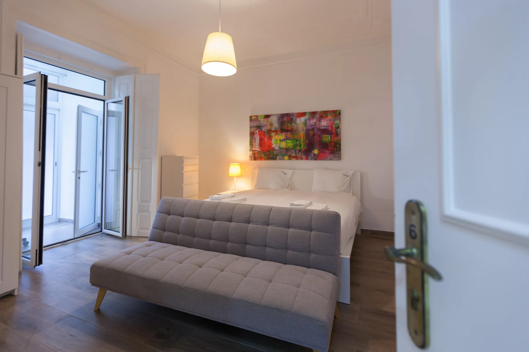 A bedroom with a bed, a cushioned bench, and colorful artwork above the bed.