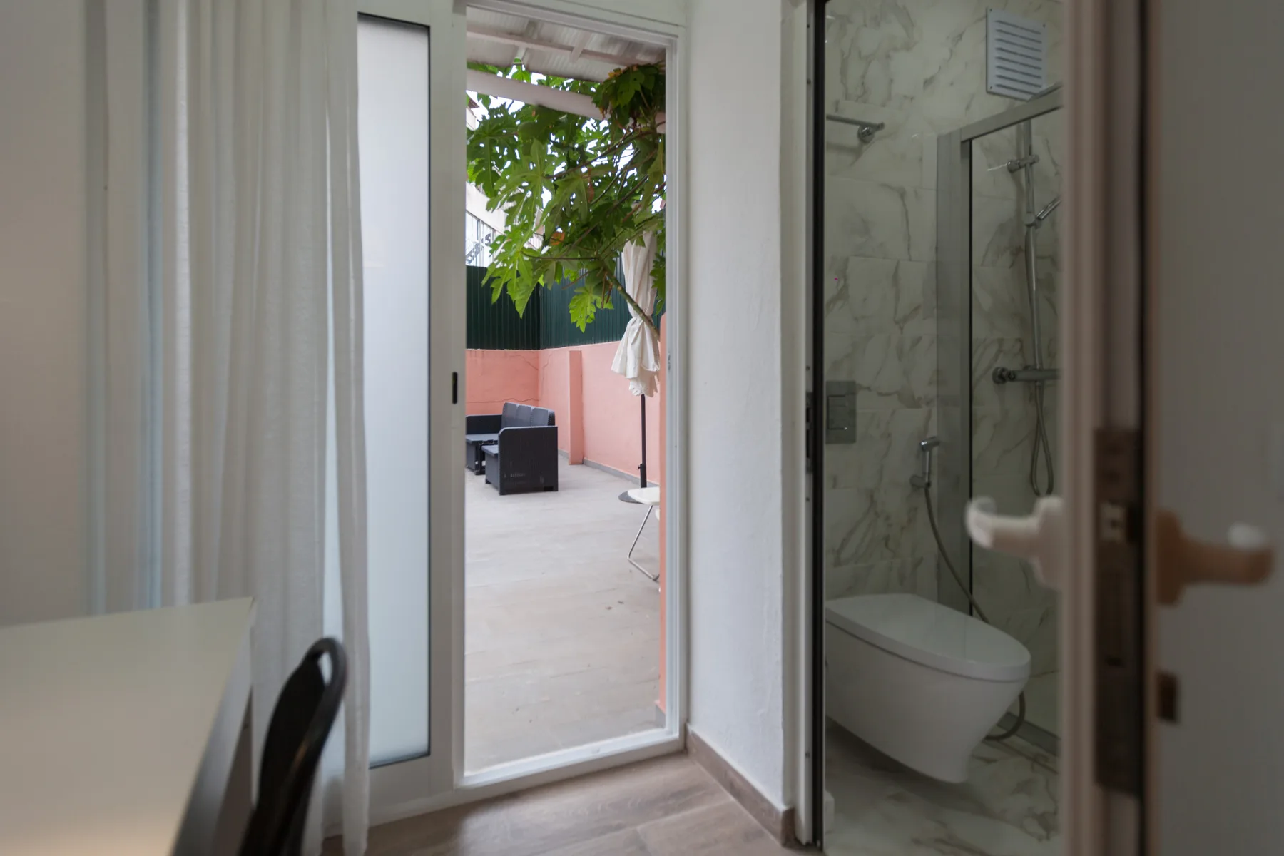 A room with an open glass door leading to a patio and a bathroom.