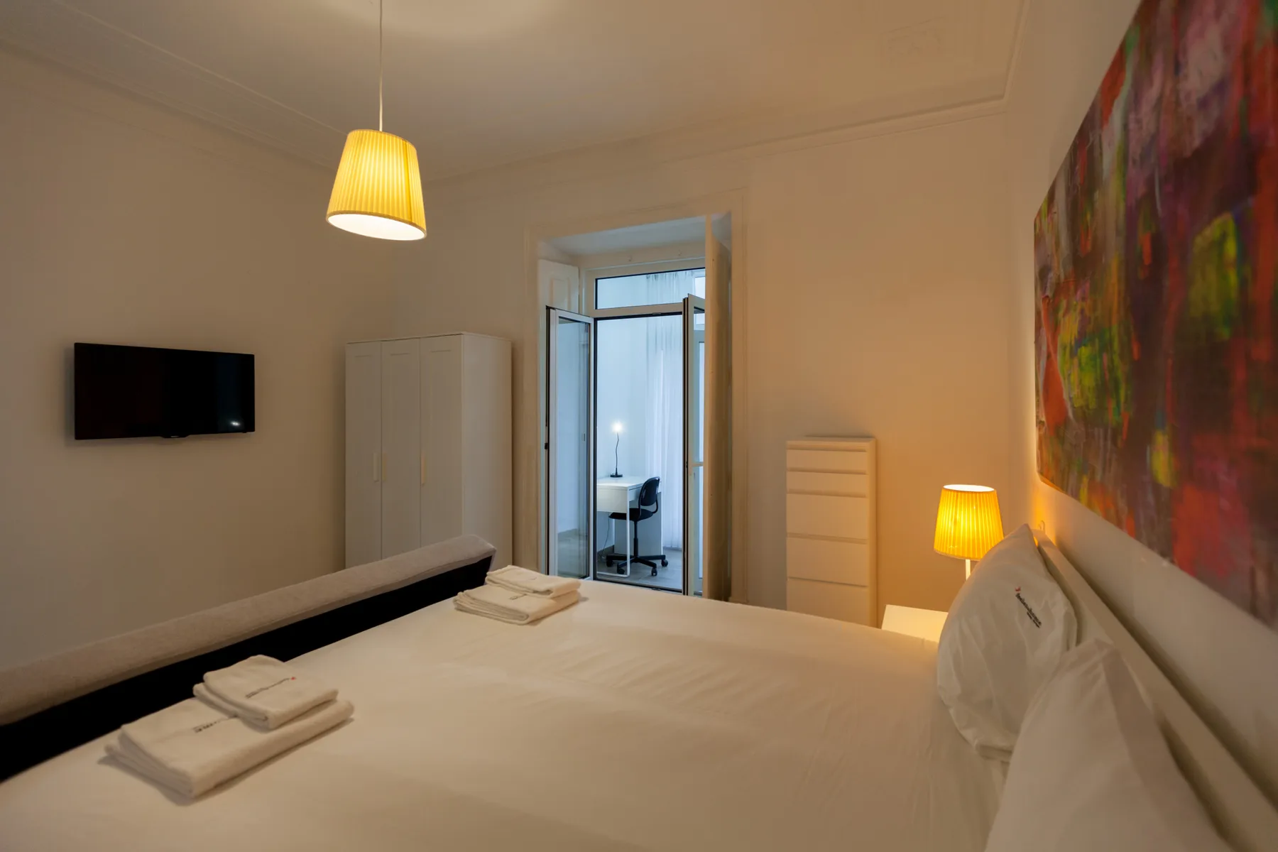 A bedroom with a neatly made bed and colorful artwork on the wall.