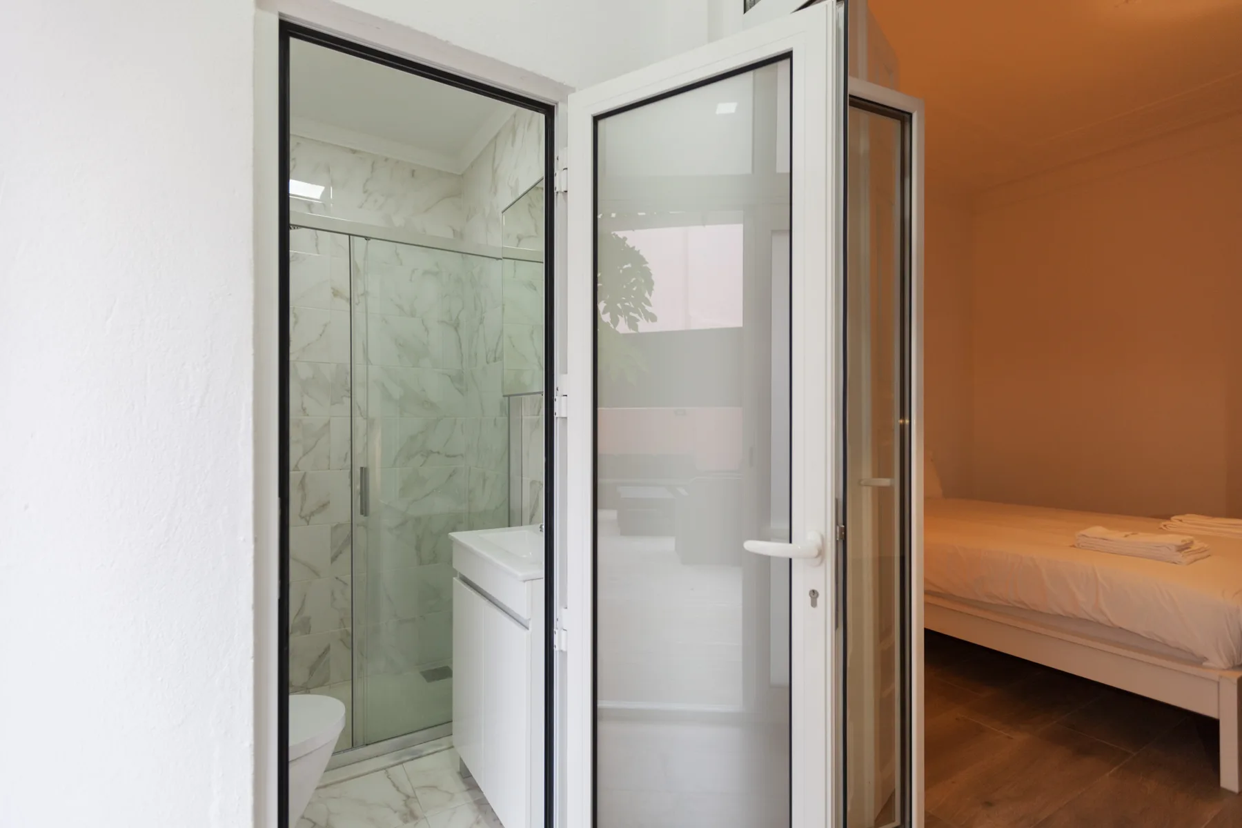 A bathroom with a glass shower beside a bedroom with a bed.