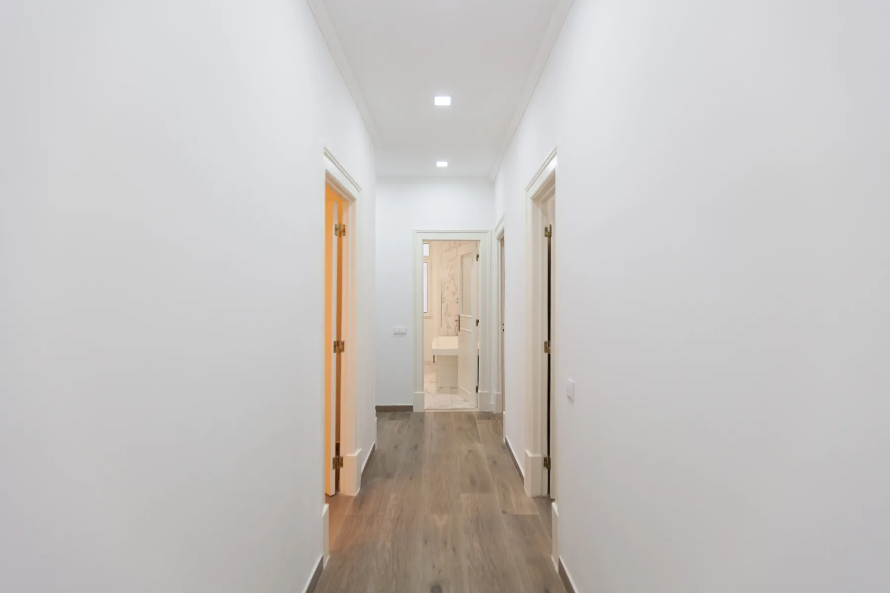 A bright hallway with several doorways and wood-look flooring.
