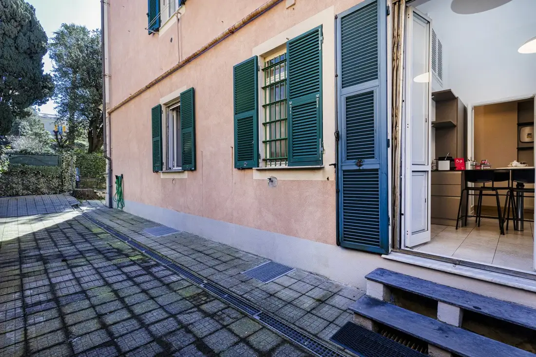 A paved patio beside a pink building, with open shutters and a doorway.