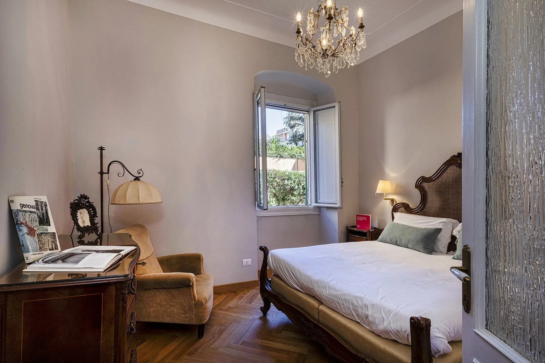 A bedroom with a bed, an armchair, and an open window.