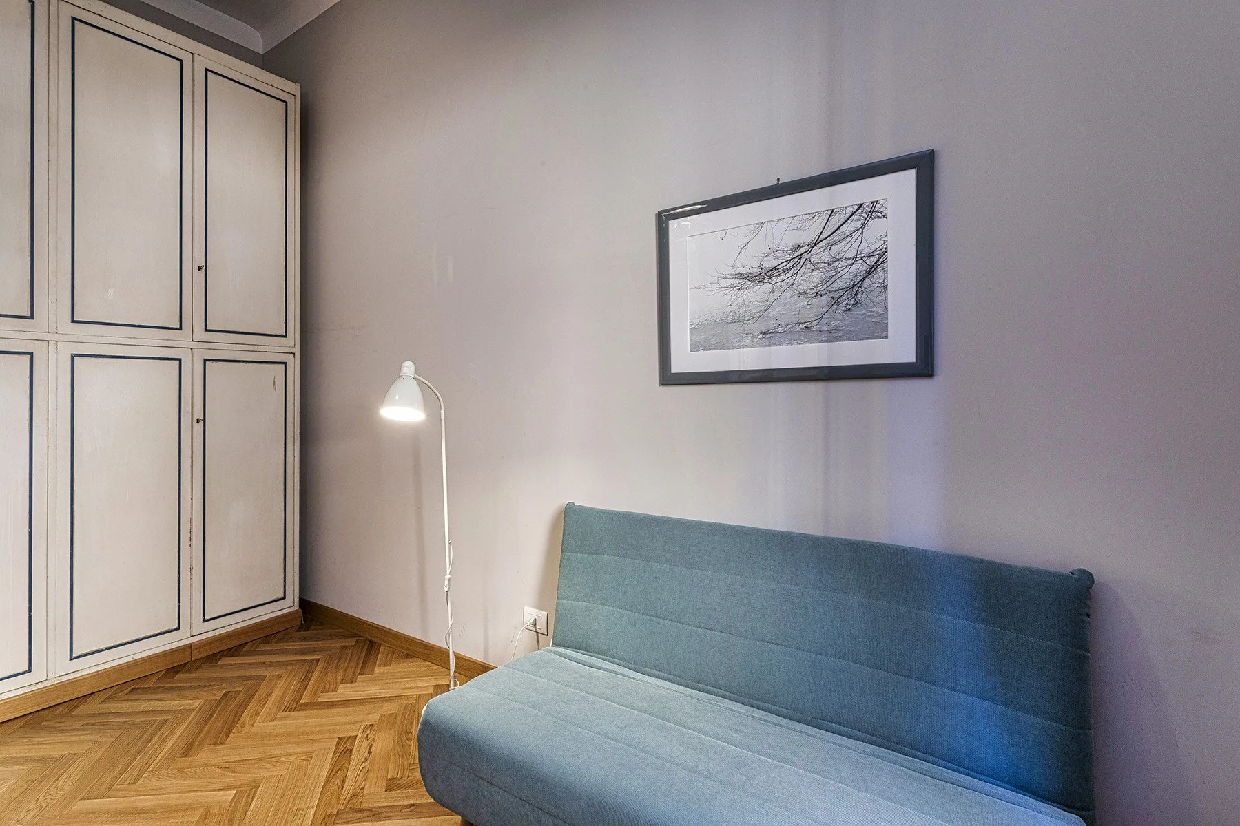 A room with a blue sofa, a floor lamp, and framed wall art.