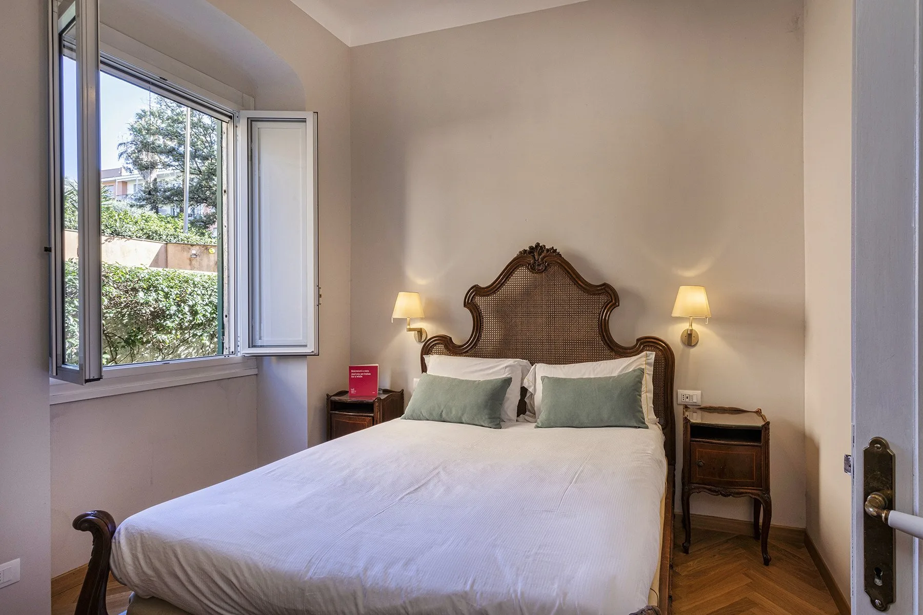 A bedroom with a double bed, bedside tables, and an open window.