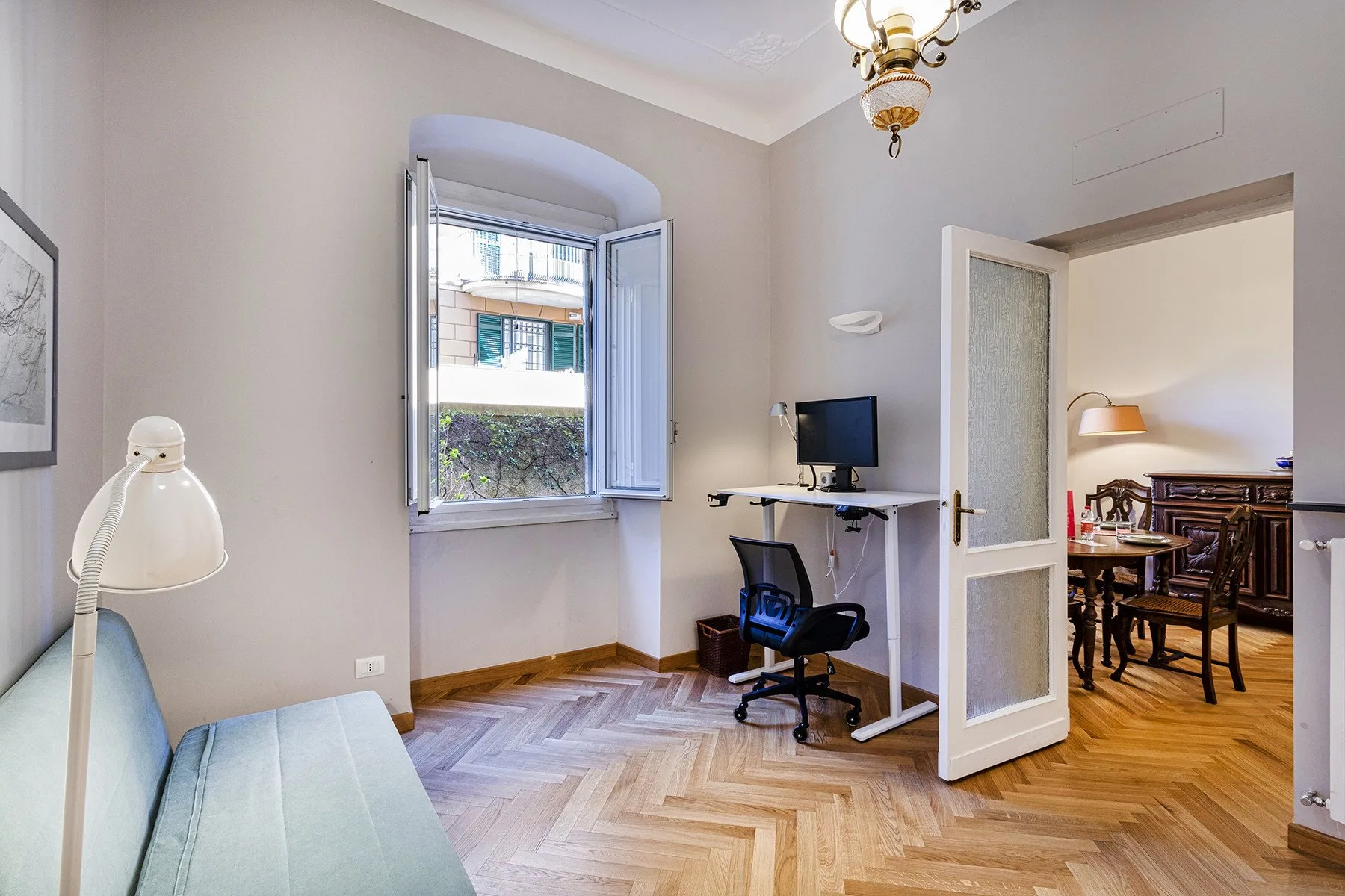 A bright room with a desk, seating, and an open doorway to a dining area.