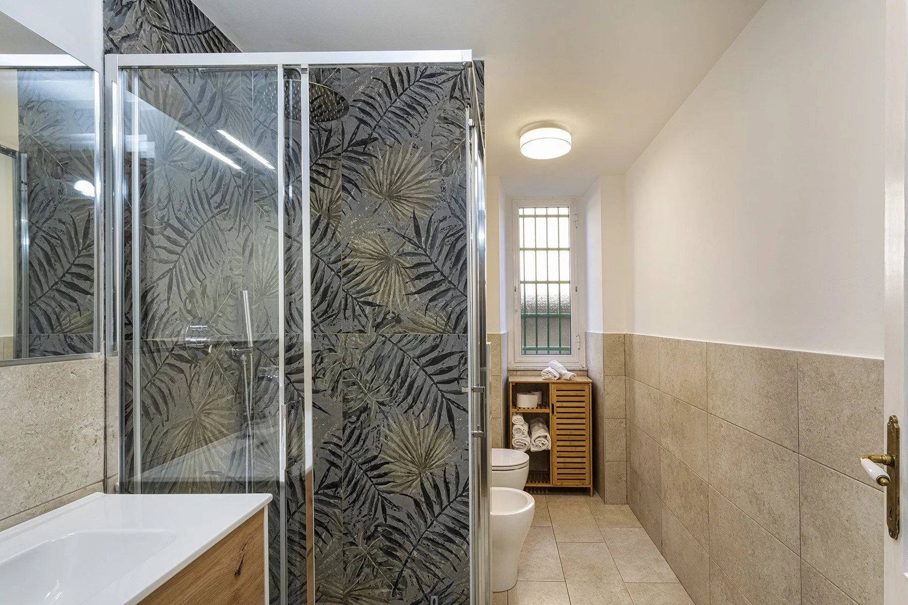 A bathroom with a glass shower and a window at the far end.