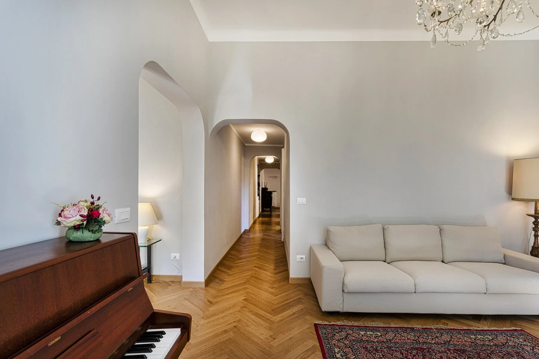 A bright living room with a piano, seating, and a hallway.
