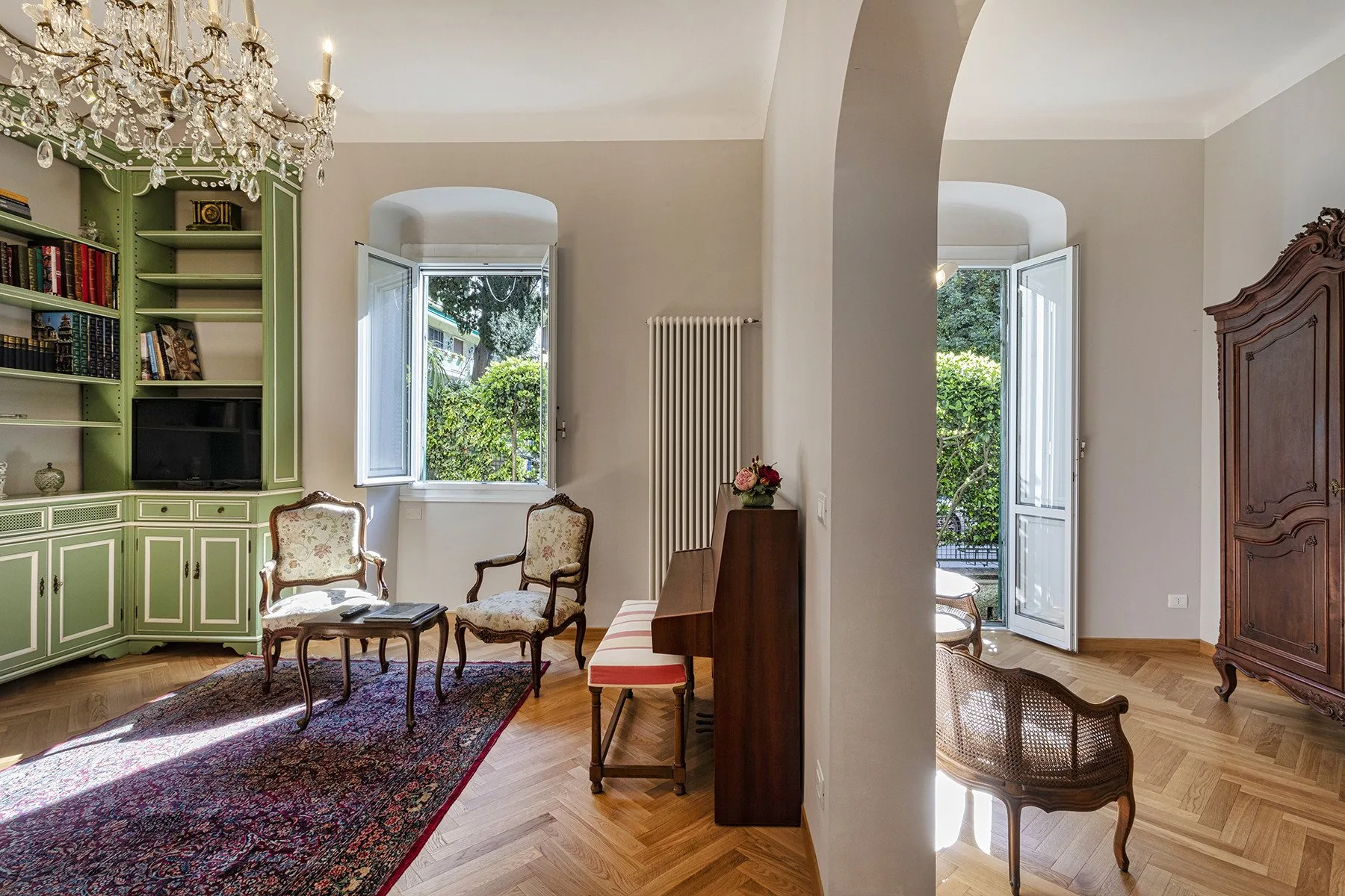 A bright living room with open windows, seating, and built-in bookshelves.