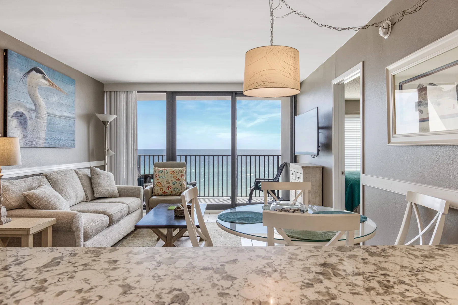 A living room with seating and a dining table faces a balcony and ocean view.
