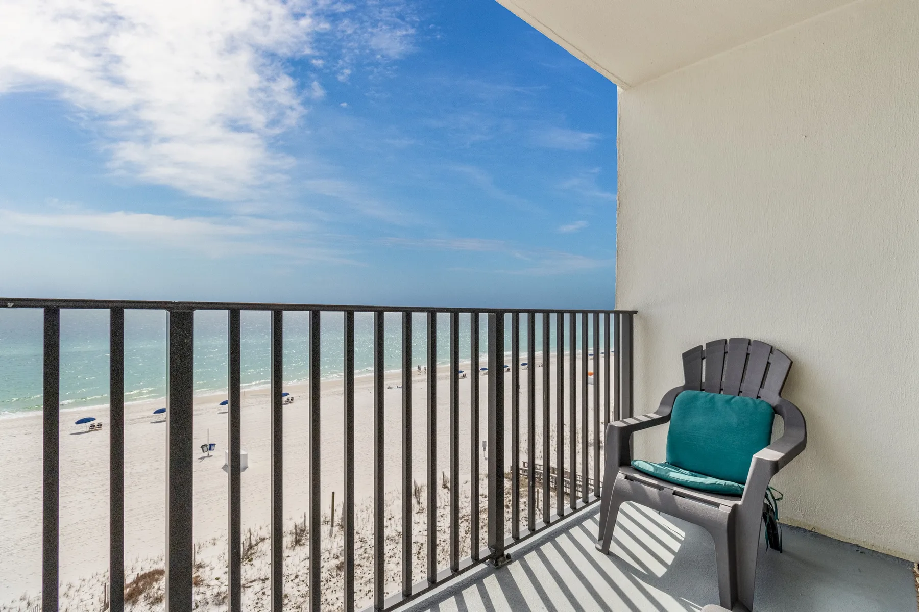 A balcony overlooking the beach, with a chair beside the railing.