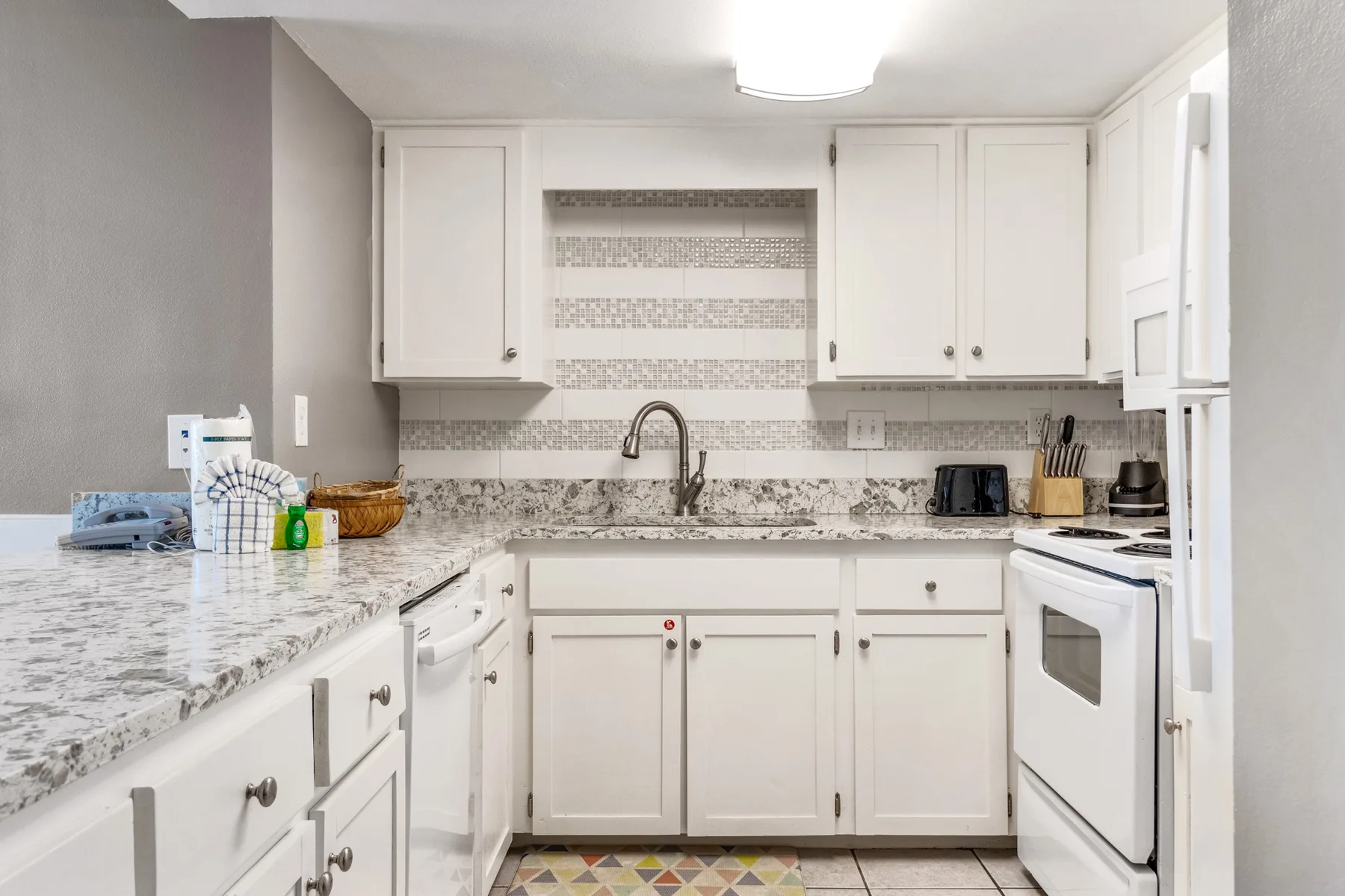 A bright kitchen with white cabinets, patterned tile, and a granite countertop.