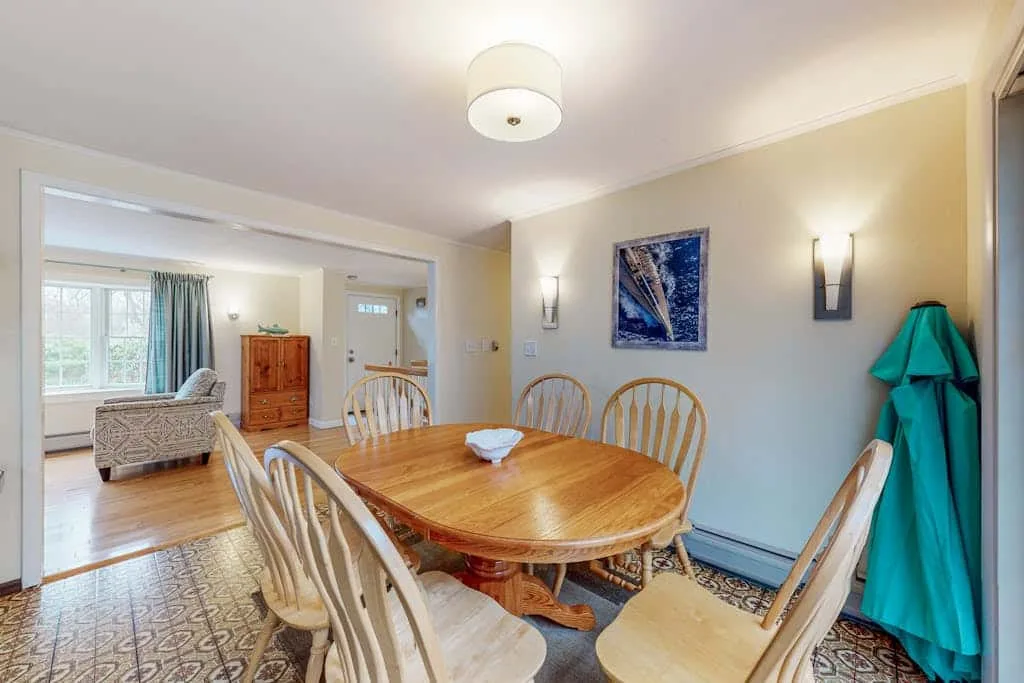 Un comedor con una mesa de madera y sillas junto a una luminosa zona de estar.