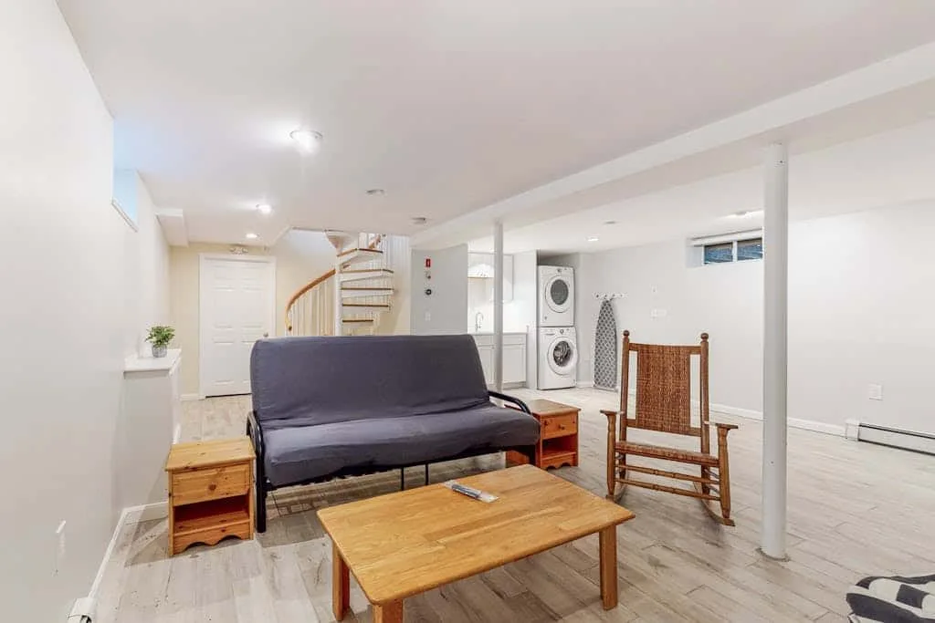 Una luminosa sala en el sótano tiene un futón oscuro y una mesa de centro de madera.