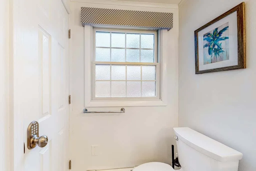 Un baño luminoso con una ventana sobre el inodoro.