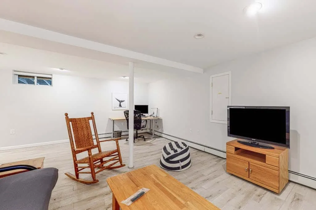Una sala amueblada en el sótano con escritorio, mecedora, televisor y mesa de centro.