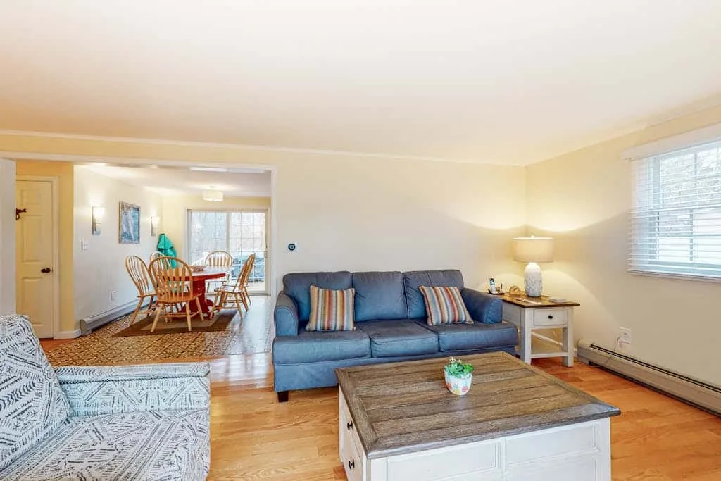 Living room with seating and a coffee table, opening onto a dining area.
