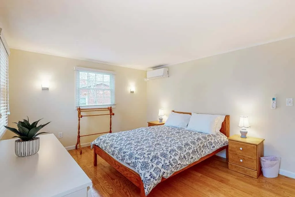 Un dormitorio con una colcha estampada, una mesita de madera y una ventana.