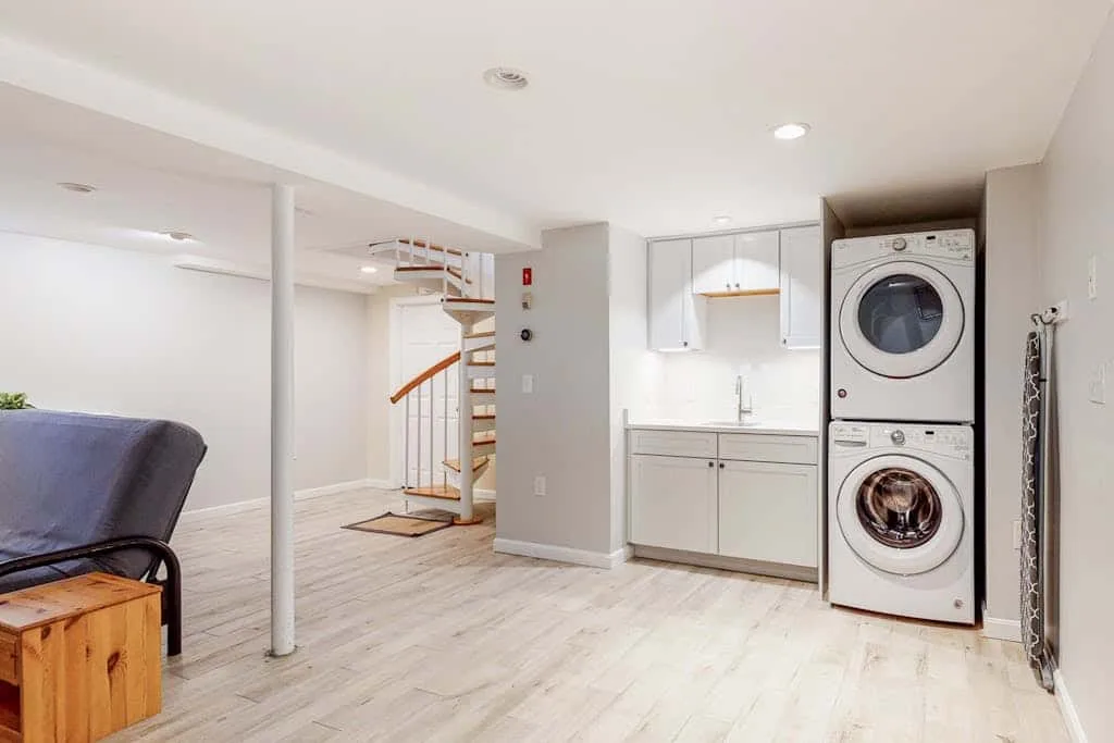 Una habitación luminosa con cocina pequeña, lavadora y secadora apiladas y espacio abierto.