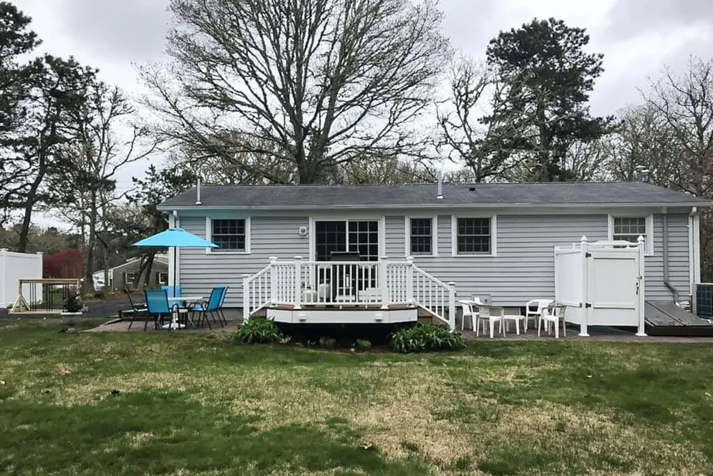 A gray house with a raised deck, outdoor seating, and a blue patio umbrella.