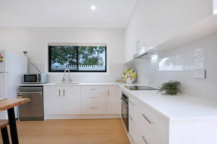 A bright white kitchen with a long counter and a window above the sink.