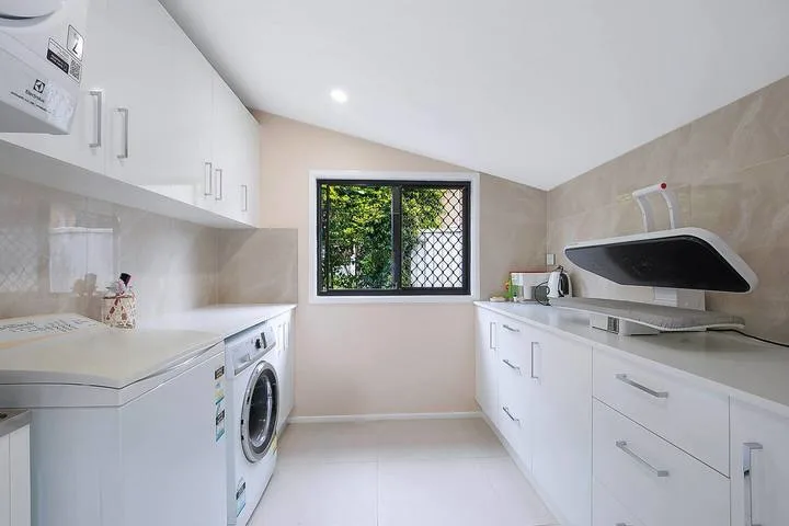 A bright laundry room with washing machines, cabinets, and a window.