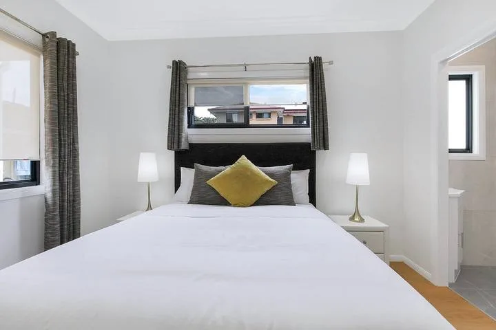A bedroom with a bed, bedside lamps, and curtained windows.