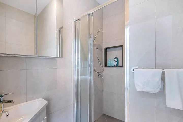 A tiled bathroom with a glass shower and a sink.