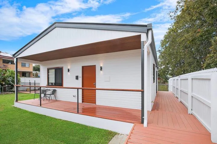 A small modern house with a covered wooden deck beside a green lawn.