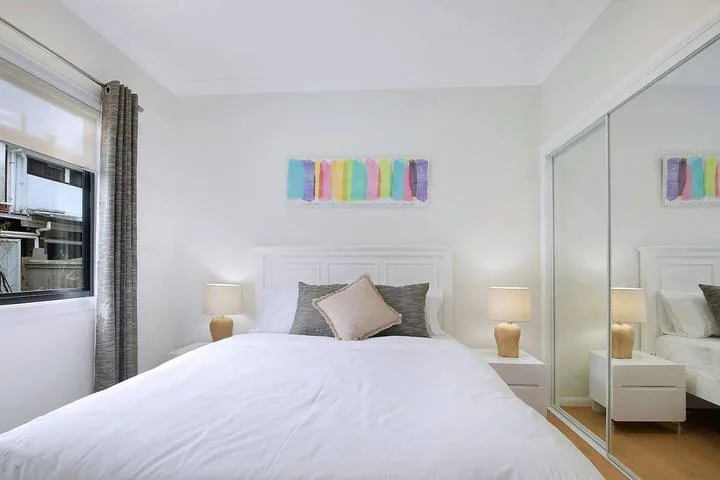 A bright bedroom with a bed, bedside tables, and colorful wall art.