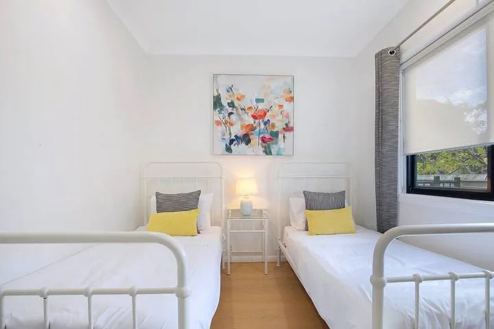 A bright bedroom with two single beds and colorful artwork on the wall.