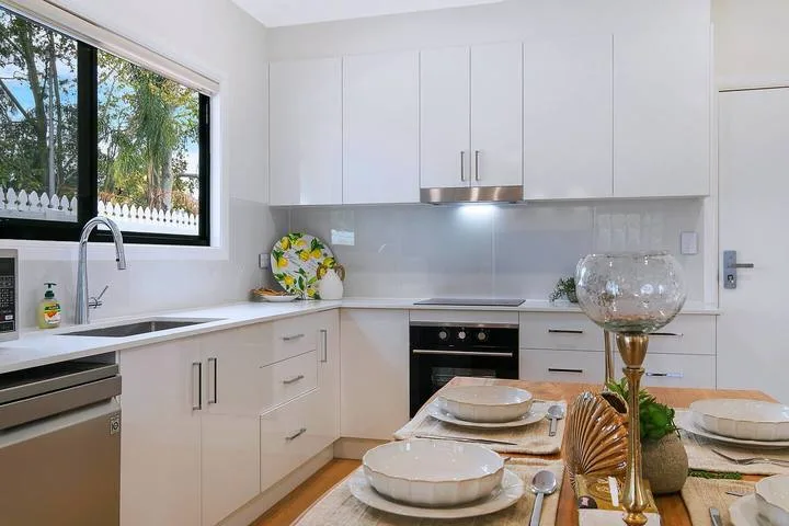 A bright kitchen with white cabinets, a countertop, and a window overlooking greenery.