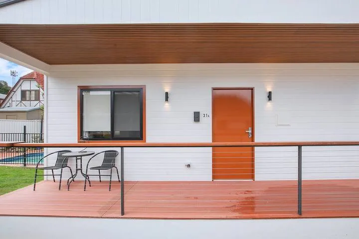 A covered outdoor deck with seating, a railing, and a door along the wall.