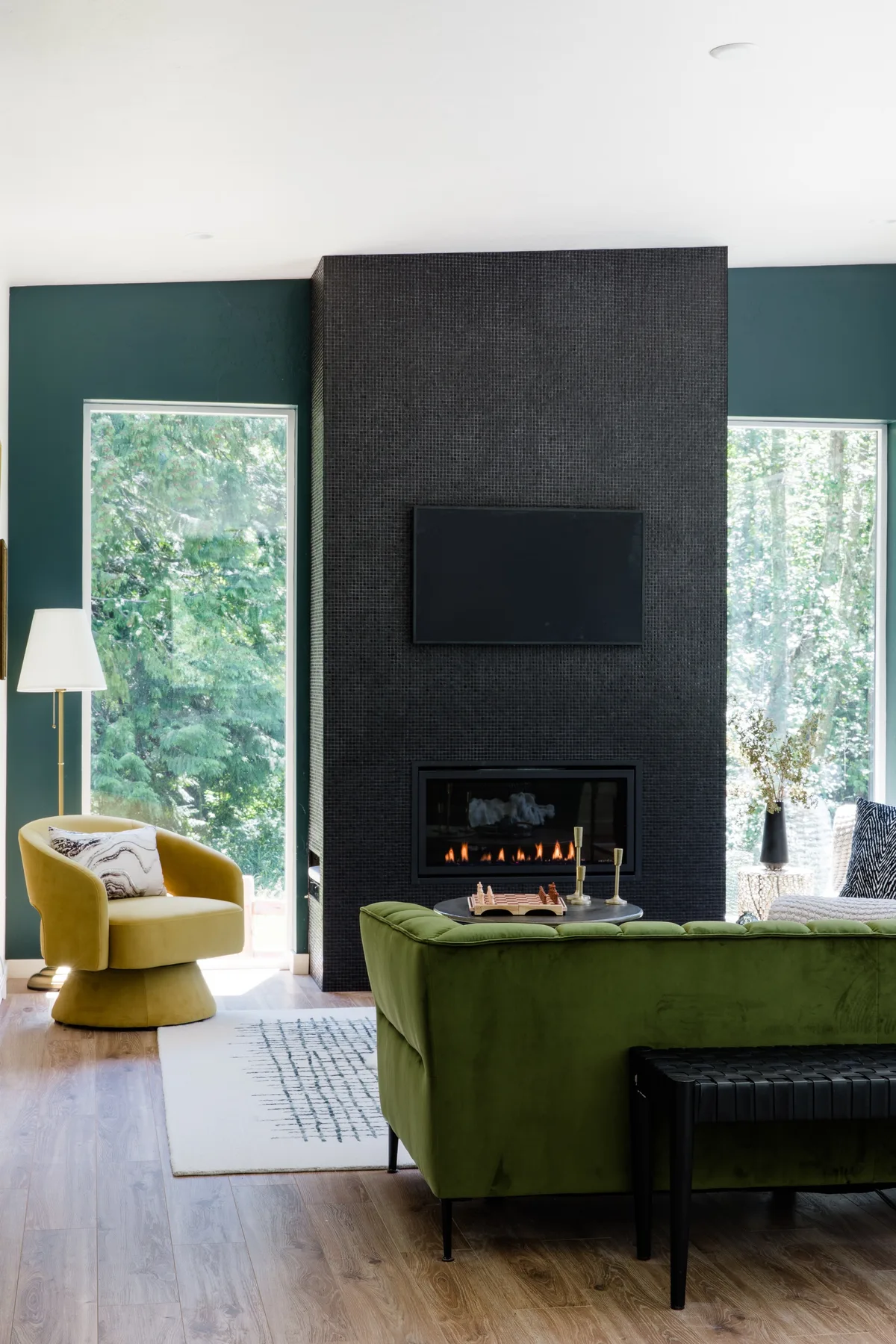 Una sala de estar moderna cuenta con asientos verdes y una chimenea bajo un televisor montado en la pared.